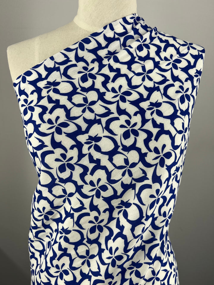 A mannequin draped with a piece of Designer Rayon - Ultramarine - 140cm fabric from Super Cheap Fabrics featuring a bold, intricate pattern of white and navy blue flowers. The vibrant floral design is repetitive and covers the entire visible area of this versatile fabric, its neutrality amplifying the fabric's stunning prints.
