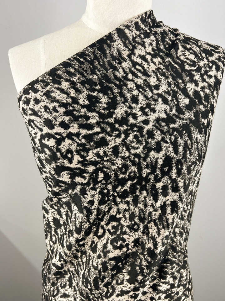 Close-up of a mannequin draped in Super Cheap Fabrics' Textured Knit - Leopard - 145cm. The medium weight fabric showcases an abstract leopard spot pattern in black and white, crafted with a slightly textured knit material that wraps over one shoulder, creating a dynamic visual effect.