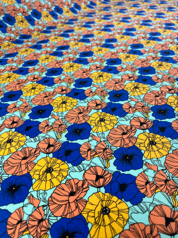 Introducing "Printed Canvas - Wonderland - 145cm" by Super Cheap Fabrics: A vibrant linen-cotton blend fabric adorned with a striking floral pattern of intricately detailed clusters of blue, yellow, and orange flowers set against a light turquoise background. This medium to heavy weight fabric design creates a colorful and lively tapestry perfect for home décor projects.