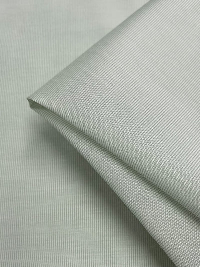 A close-up image of neatly folded, light-weight Designer Silk - Prodigy - 158cm in a solid color from Super Cheap Fabrics. The material appears to have a subtle, textured pattern with fine vertical lines, giving it a slightly ribbed surface. Ideal for dresses, the fabric looks smooth and well-ironed.
