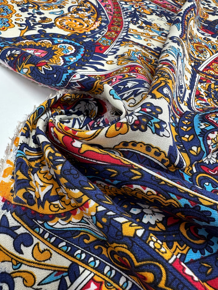 A close-up of Super Cheap Fabrics’ Bamboo Rayon - Moroccan (150cm), featuring ornate blue, yellow, red, and white paisley and floral designs. The lightweight fabric is slightly wrinkled, showing textured folds on its surface.
