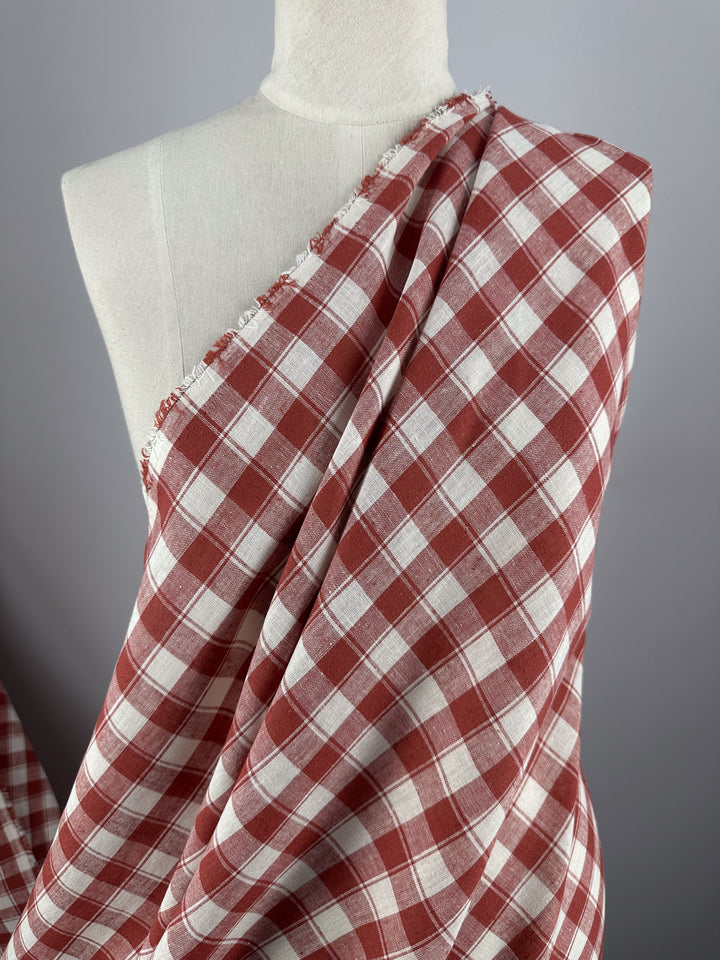 A lightweight dress form is draped with Super Cheap Fabrics' Linen Blend - Cranberry Check (145cm), featuring a rust and white checkered pattern set diagonally, with a slightly frayed top edge, against a plain gray background.