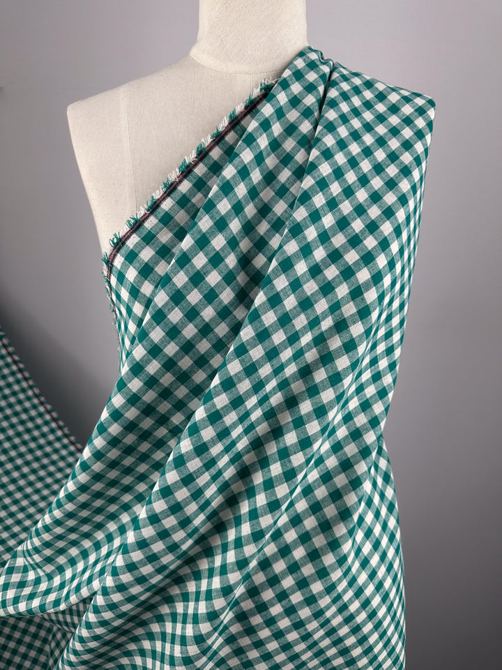 A mannequin displays Super Cheap Fabrics' Linen Blend - Verdant Gingham (145cm), featuring lightweight green and white checks with subtle red stitching, set against a neutral background.