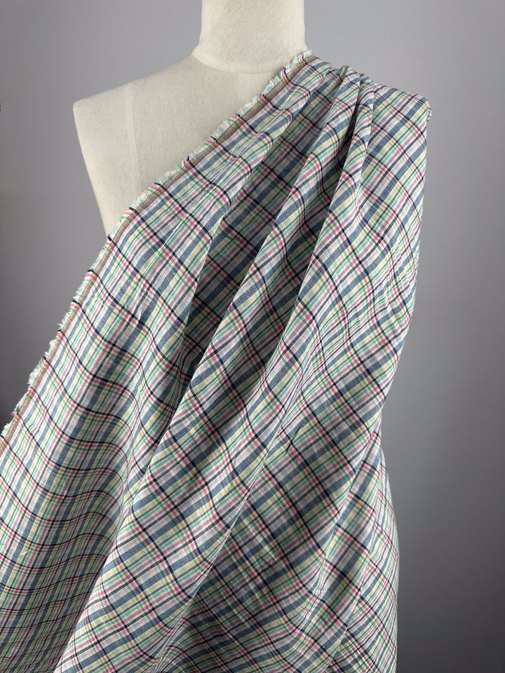 A mannequin displays Super Cheap Fabrics' Linen Blend - Tartan Prism (140cm), featuring a lightweight, multi-plaid design in red, green, blue, and black on white, set against a plain gray backdrop.