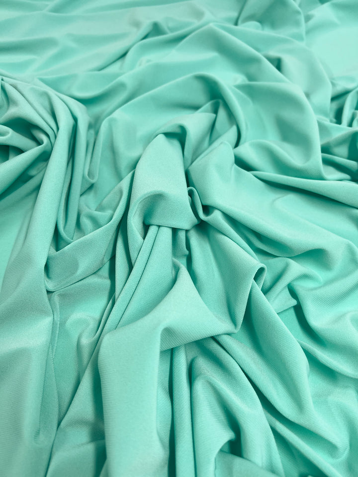 A close-up photo of crumpled, light mint green satin fabric. The medium weight material showcases a smooth and shimmering texture, with soft folds and draping throughout the image, creating an elegant and luxurious appearance reminiscent of Super Cheap Fabrics' ITY Knit - Ice Blue - 150cm.