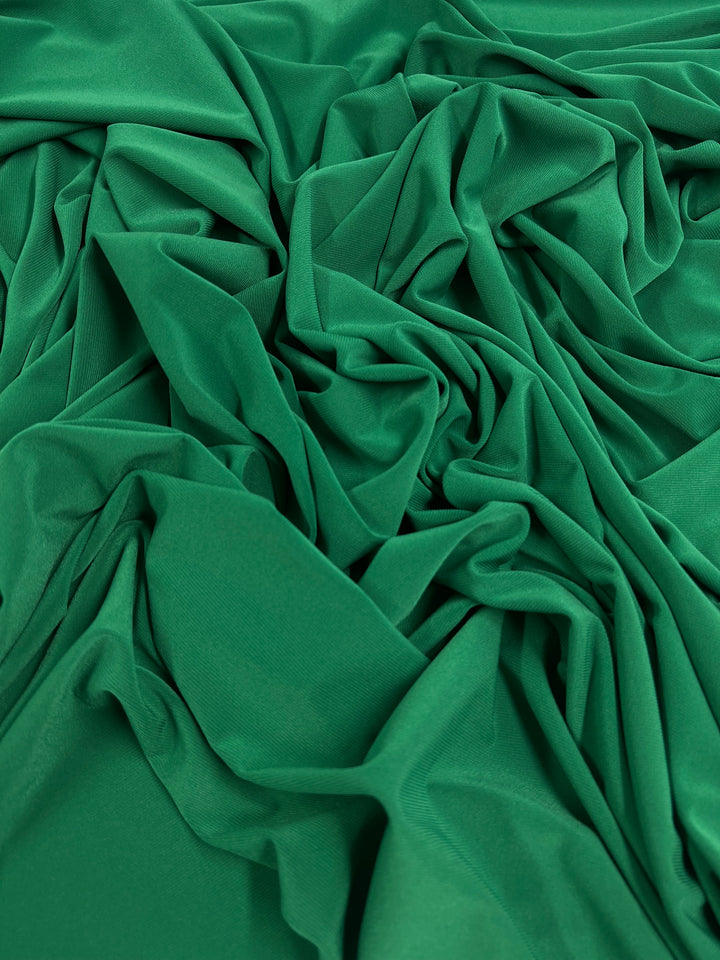 A close-up view of Super Cheap Fabrics' ITY Knit - Emerald - 150cm fabric with a smooth texture, intricately draped and wrinkled, creating a series of soft folds and shadows. The vibrant color and silky appearance suggest the medium weight fabric has great elasticity and a soft touch, making it lightweight and flowing.