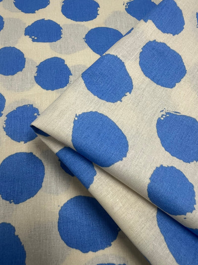 Fabric with a white background adorned with large, uneven blue circles. The blue circles have a painted look, giving a casual and artistic feel. This **Super Cheap Fabrics** **Printed Cotton - Blite Dots - 150cm** fabric, made from natural cotton fibers, is folded neatly in one section and ideal for clothing and household items.