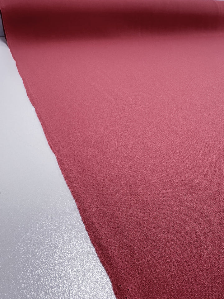 A roll of Super Cheap Fabrics' Plain Scuba Crepe in Holly Berry is laid flat, stretching top to bottom. The medium-weight, textured material's edges are slightly uneven, showcasing its 150cm width.