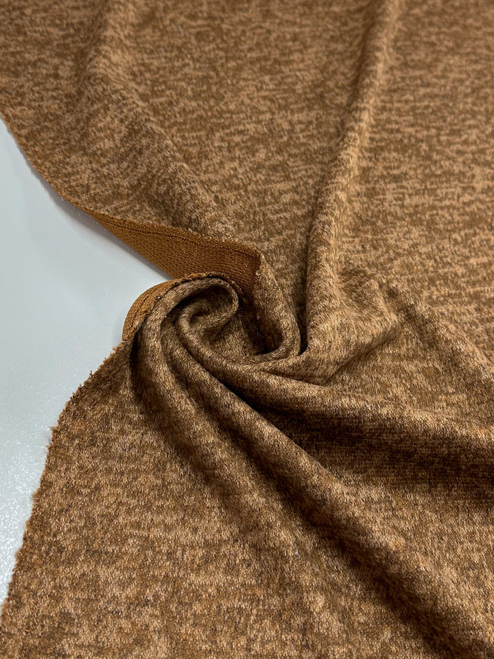 A close-up of Super Cheap Fabrics’ Textured Knit - Foxtrot (155cm) reveals its soft, brown heathered look and flexible drape, with the medium weight fabric partially rolled and folded on a white surface.