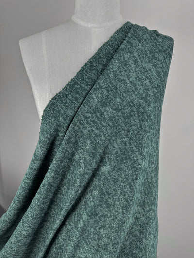 A mannequin showcases Super Cheap Fabrics' Textured Knit - Mallard Green - 160cm, draped over one shoulder and flowing diagonally across the torso, highlighting its comfort against a neutral background.