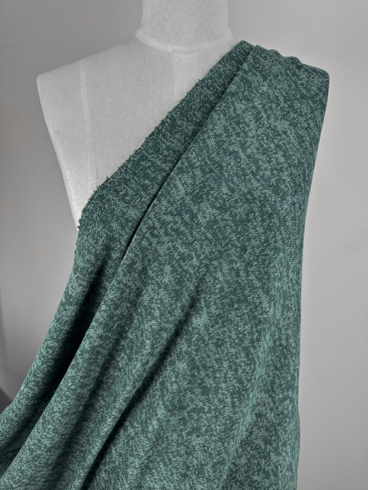 A mannequin showcases Super Cheap Fabrics' Textured Knit - Mallard Green - 160cm, draped over one shoulder and flowing diagonally across the torso, highlighting its comfort against a neutral background.
