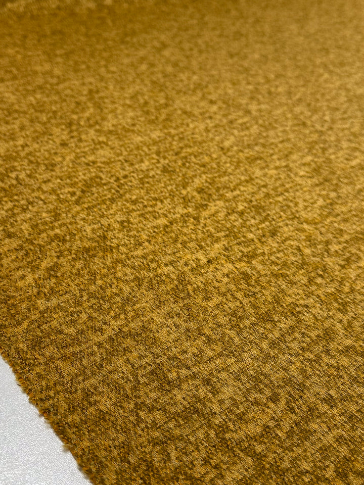 A close-up of Super Cheap Fabrics' Textured Knit - Honey Gold - 155cm shows its soft, medium weight knit and subtle mottled color, with the textured fabric edge visible in the lower left corner.