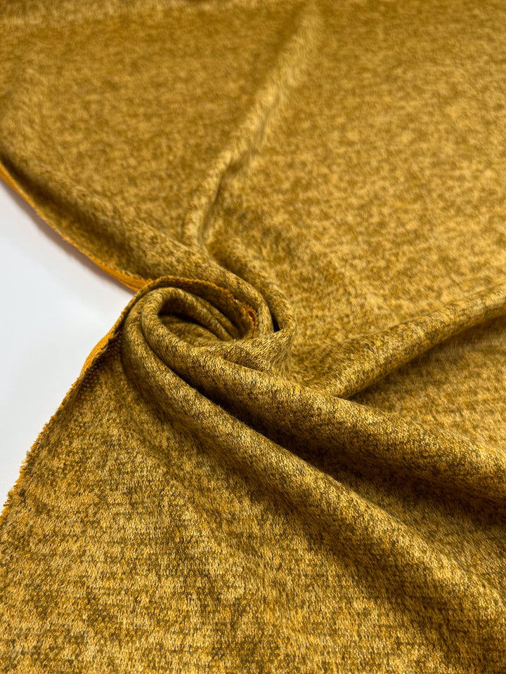 A close-up of Super Cheap Fabrics’ Textured Knit - Honey Gold - 155cm, softly draped and twisted on a flat surface to showcase its cozy, medium weight feel and subtle heathered look.