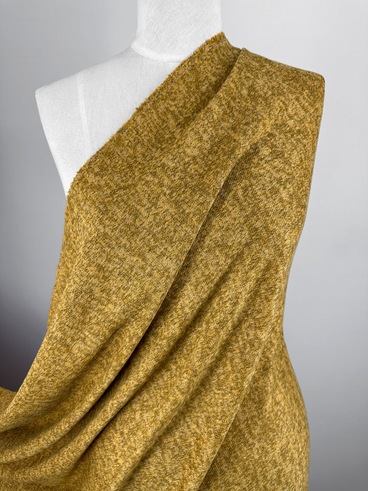 A dress form displays Super Cheap Fabrics’ Textured Knit - Honey Gold - 155cm, a medium weight heathered fabric, arranged to highlight its drape and texture against a plain light gray background.