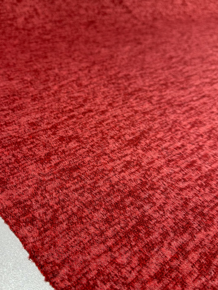A close-up of Super Cheap Fabrics' Textured Knit - Rococco Red (150cm) shows its soft, slightly fuzzy, medium-weight fabric with a subtle mottled pattern. A smooth, light surface appears in the bottom left corner.