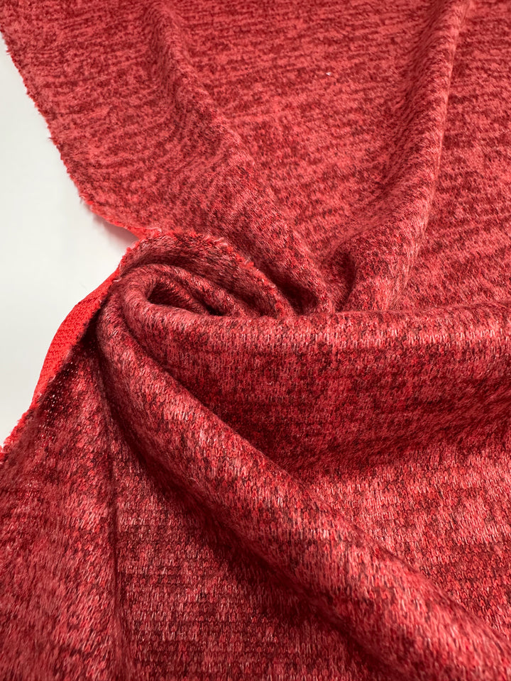 Close-up of Super Cheap Fabrics’ Textured Knit - Rococco Red (150cm): a heathered red medium weight knit with a soft, slightly fuzzy finish. Loosely folded to highlight its generous stretch, flexibility, and detailed knit pattern.