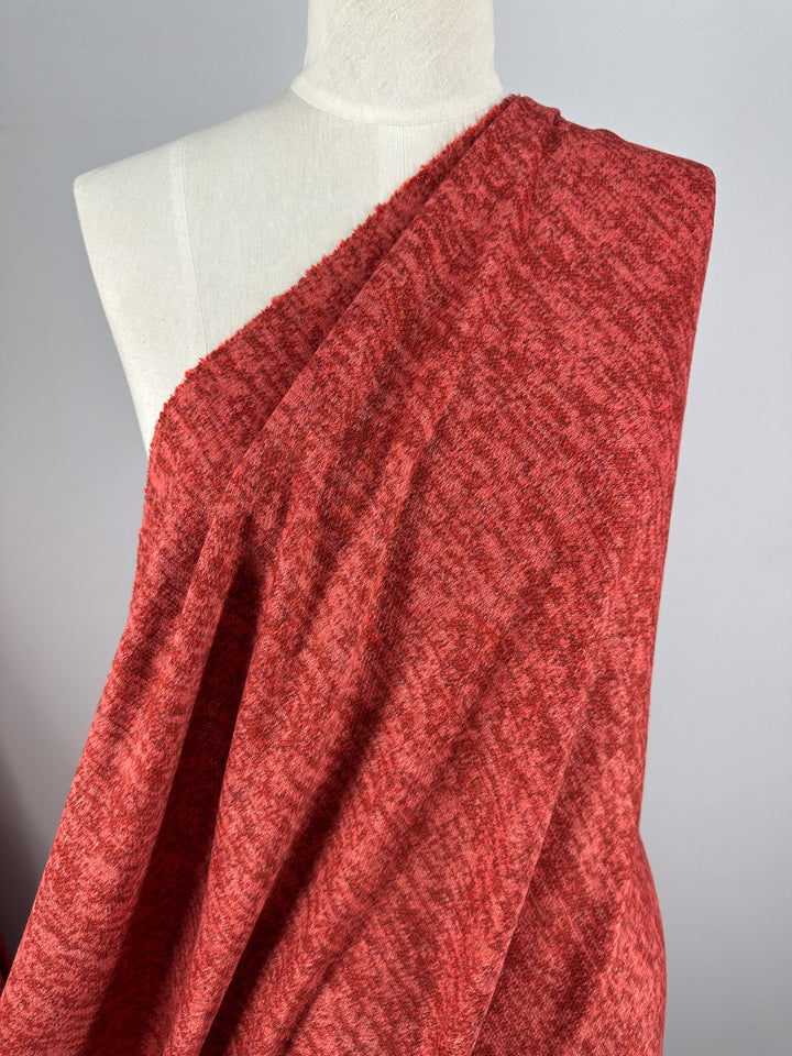 A mannequin displays Super Cheap Fabrics’ Textured Knit - Rococco Red - 150cm, a stretchy, textured red fabric, draped over one shoulder against a plain light gray background.