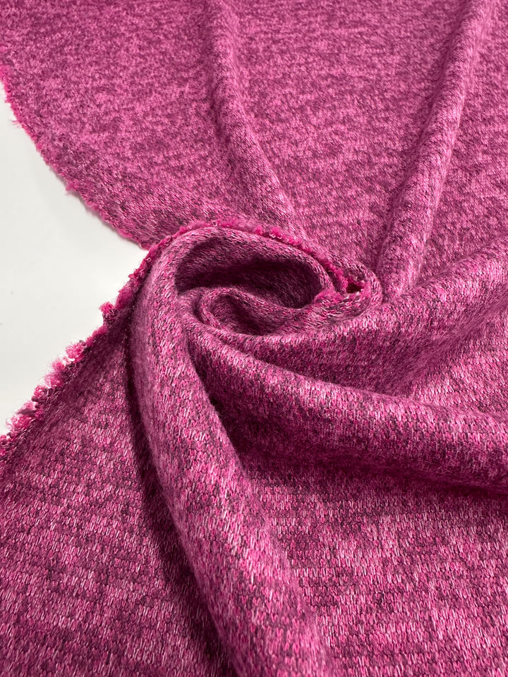 A close-up of Super Cheap Fabrics' Textured Knit - Rose Violet - 150cm shows the medium-weight fabric in soft folds and a spiral, with unfinished edges on the left, set against a white background.