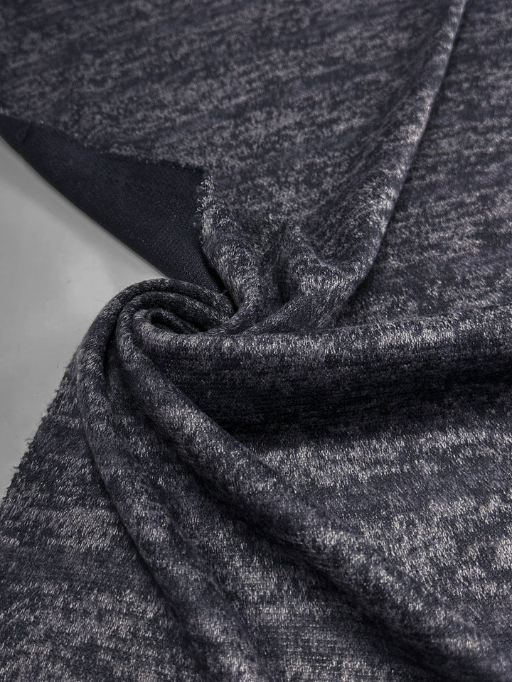 A close-up of Super Cheap Fabrics' Textured Knit - Ink Marle - 150cm, showing its heathered dark gray texture twisted into a swirl with a soft, touchable surface on display.