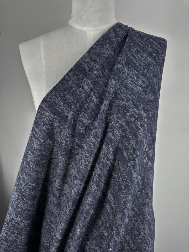 A gray mannequin displays Super Cheap Fabrics' Textured Knit - Ink Marle - 150cm, a soft, dark blue and gray marbled fabric, set against a plain light gray background.