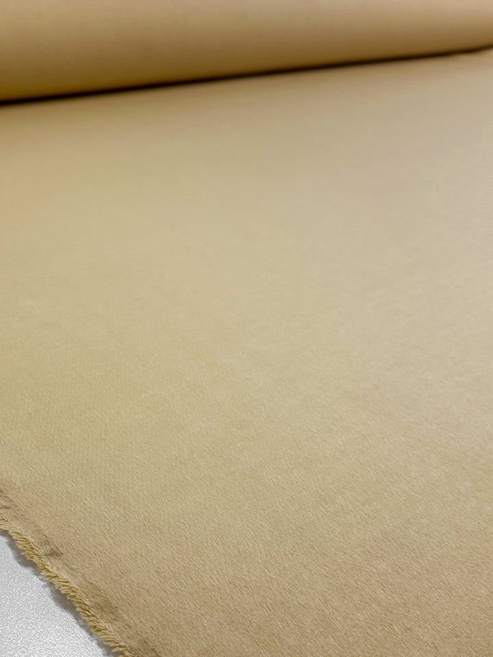 A close-up of Super Cheap Fabrics' Wool Cashmere - Banana - 150cm showcases its smooth texture, luxurious softness, beige hue, and a slightly frayed edge as it lies spread on a flat surface.