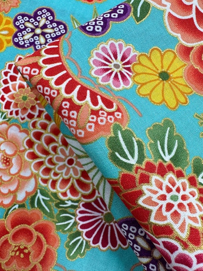 Super Cheap Fabrics' Japanese Printed Cotton - Turquoise Blossom - 112cm features vibrant red, yellow, purple, and pink floral designs on turquoise—ideal for standout sewing projects. Slight folds highlight its intricate patterns.
