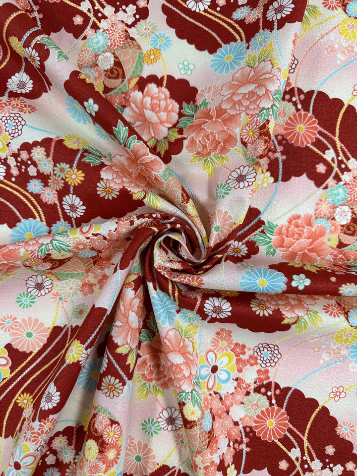 A close-up of Super Cheap Fabrics' Japanese Printed Cotton - Textured Crane Garden (112cm), showing a swirled fold and vibrant red, pink, blue, and yellow floral motifs with fine details on a light background.