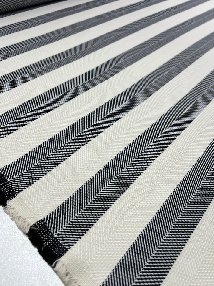 A close-up of Super Cheap Fabrics' Upholstery Herringbone - Salt & Pepper - 140cm features alternating black and off-white vertical stripes. The black stripes have a herringbone pattern, adding texture and visual interest. The durable fabric appears to be spread out, showcasing its pattern and material.