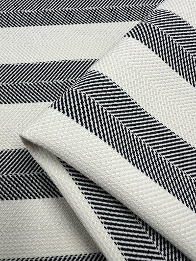 A close-up image of upholstery fabric with a herringbone pattern. The durable fabric, Upholstery Herringbone - Salt & Pepper - 140cm by Super Cheap Fabrics, features alternating black and white diagonal stripes, creating a zigzag effect throughout.