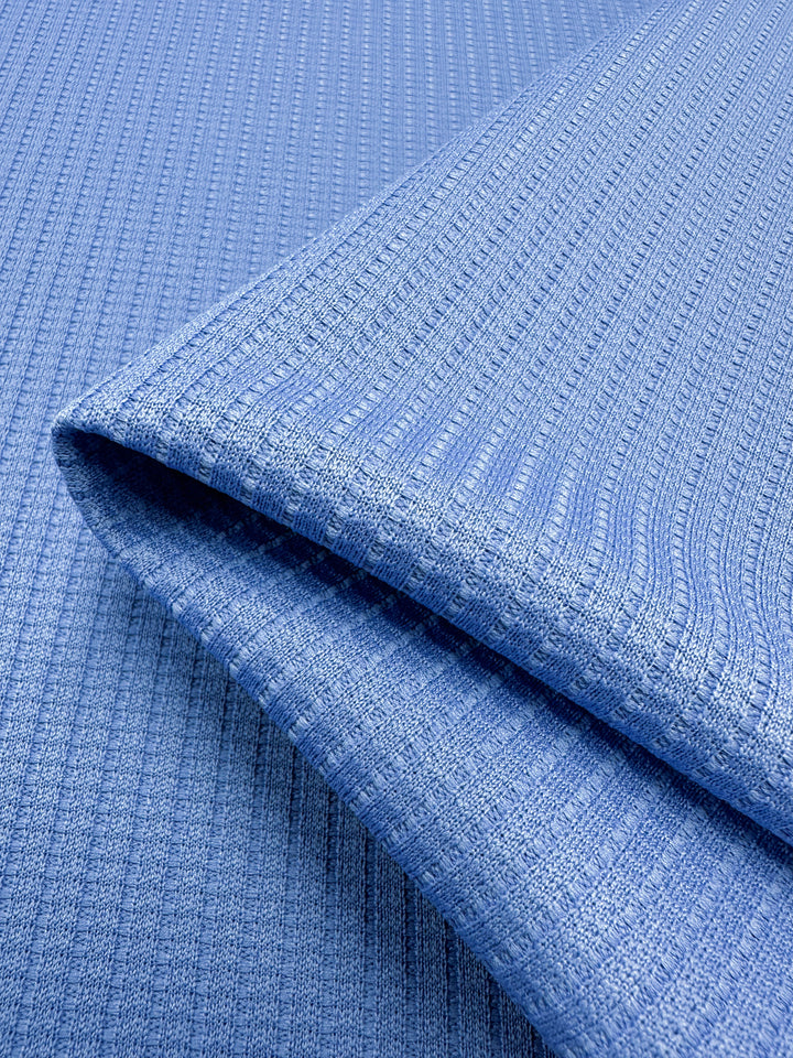 Close-up of neatly folded Textured Knit - Ultramarine from Super Cheap Fabrics, displaying its subtle ribbed texture. The polyester fabric appears soft and slightly stretchy, with visible vertical lines accentuating the textile pattern. The image focuses on the detailed surface and weave of this medium weight fabric that spans 155cm in width.