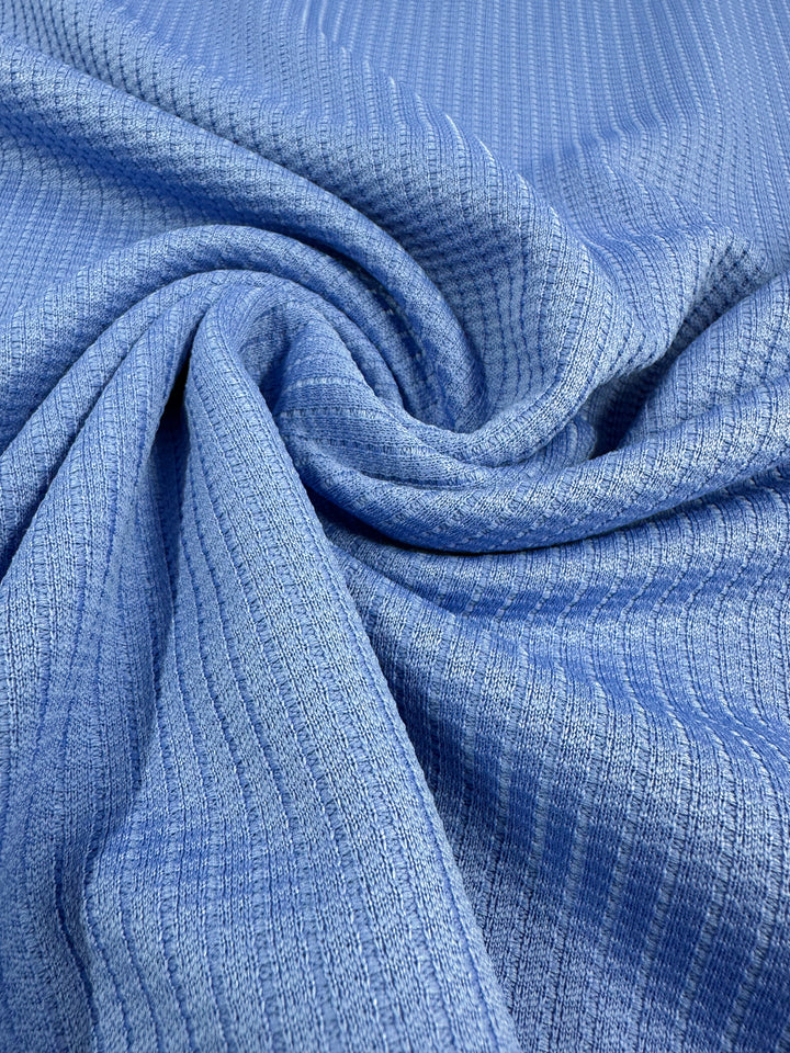 Close-up of the Textured Knit - Ultramarine from Super Cheap Fabrics, a medium weight fabric with a subtle ribbed texture. The cloth is slightly gathered and twisted in the center, creating soft folds and shadows that highlight the texture and drape of the 155cm wide material.