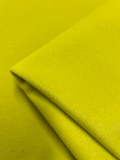 An image of a folded piece of fabric in a bright, vibrant yellow color perfect for outer coats. The Wool Cashmere - Celery - 150cm by Super Cheap Fabrics appears smooth and soft, with a slight sheen. The fold creates clean, crisp lines, adding depth and texture to the image.