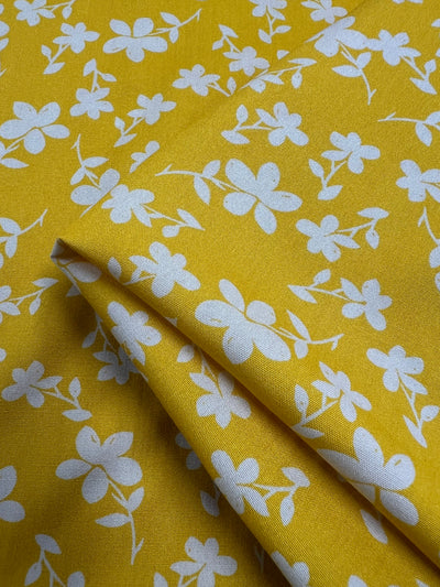 A close-up image of a colourful fabric adorned with a pattern of white floral designs. The Super Cheap Fabrics Printed Rayon - Yellow Jasmine - 145cm appears to be folded neatly, showcasing both the front and the underside of the material. The flowers are small and distributed evenly across the vibrant prints.