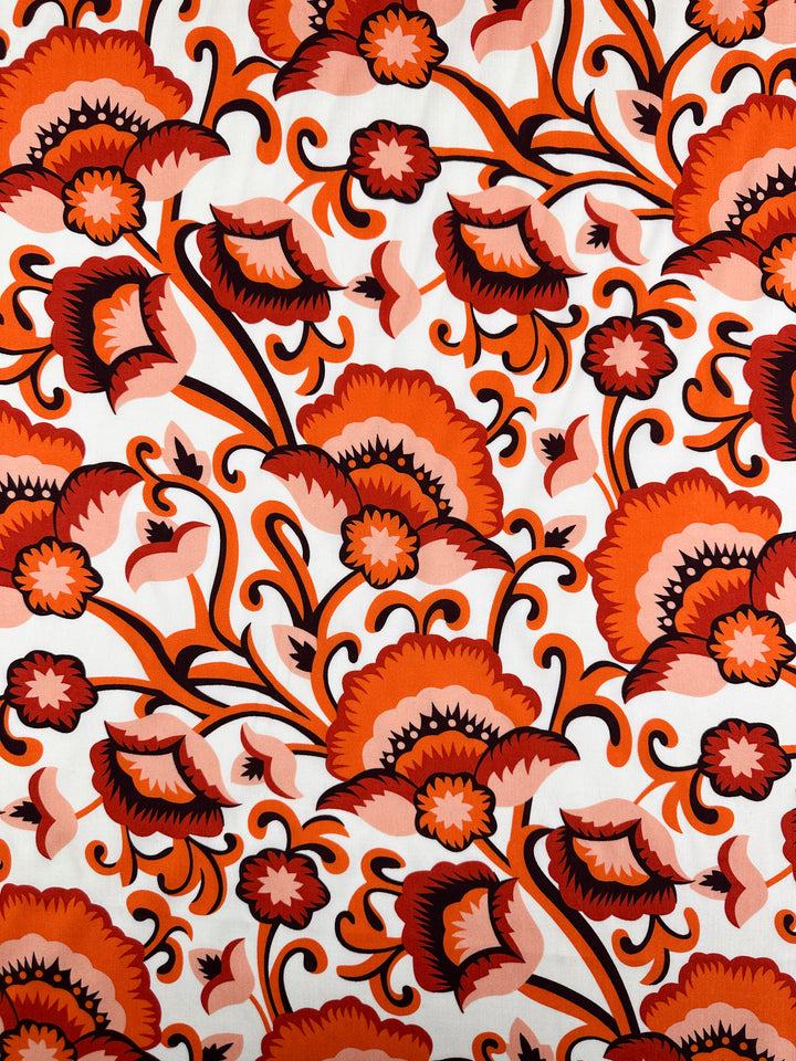 Designer Rayon - Floral Delight - 145cm from Super Cheap Fabrics features a bold, symmetrical floral pattern with red, orange, and pink flowers on white rayon—ideal for vibrant, versatile clothing.