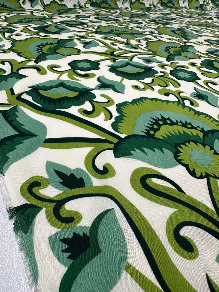 Close-up of Designer Rayon - Verdant Bloom (145cm) by Super Cheap Fabrics, featuring a bold cream backdrop with vibrant green floral prints and swirling leafy stems.