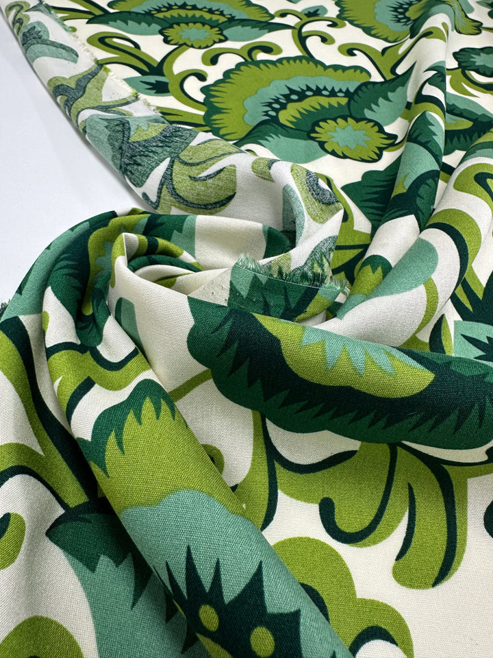 A close-up of Super Cheap Fabrics' Designer Rayon - Verdant Bloom (145cm), featuring a bold retro floral pattern in green shades on white, draped and softly folded—a vibrant, versatile fabric for unique creations.