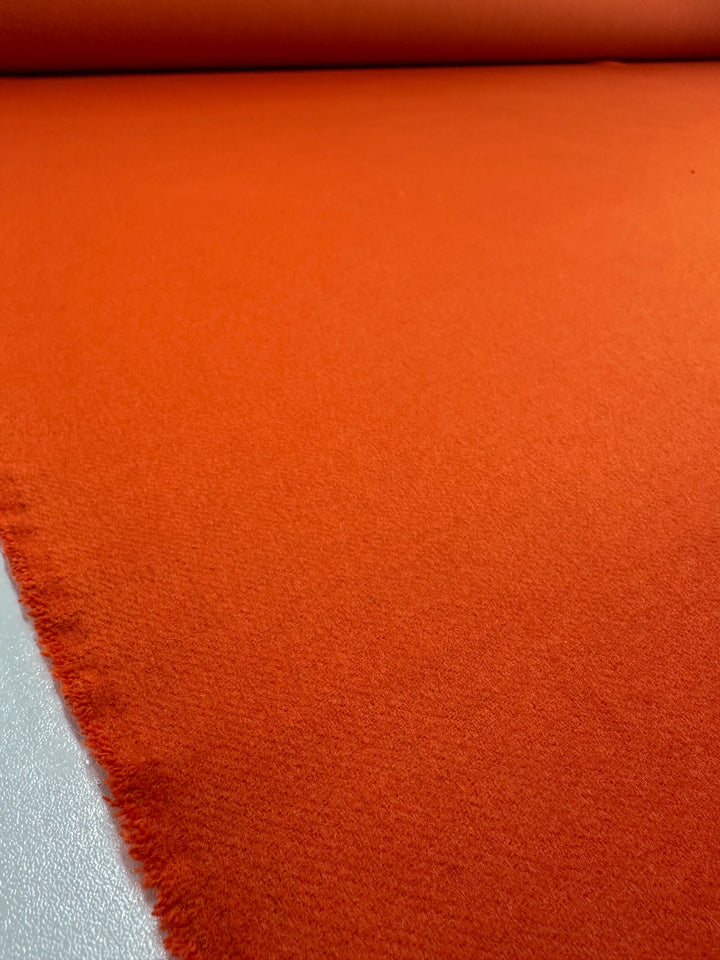 A close-up of Wool Cashmere - Koi - 150cm by Super Cheap Fabrics shows its vibrant orange hue, heavy weight, and soft, slightly fuzzy texture with a neatly cut edge displayed on a flat surface.