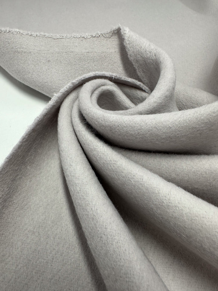 Close-up of Super Cheap Fabrics' Wool Cashmere - Gray Morn (150cm), featuring soft, light gray wool cashmere fabric with a smooth, fuzzy texture, elegantly folded to highlight its luxurious softness and flexibility.