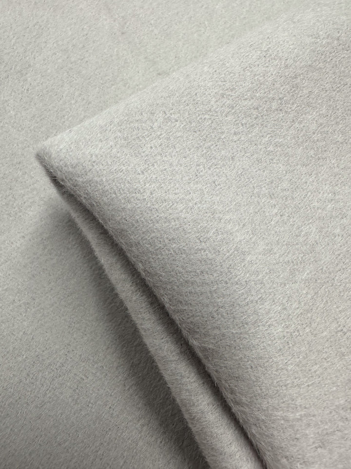 Close-up of Super Cheap Fabrics' Wool Cashmere - Gray Morn - 150cm, a soft, light gray fabric with a slightly fuzzy texture, folded on a matching surface for a luxurious look.
