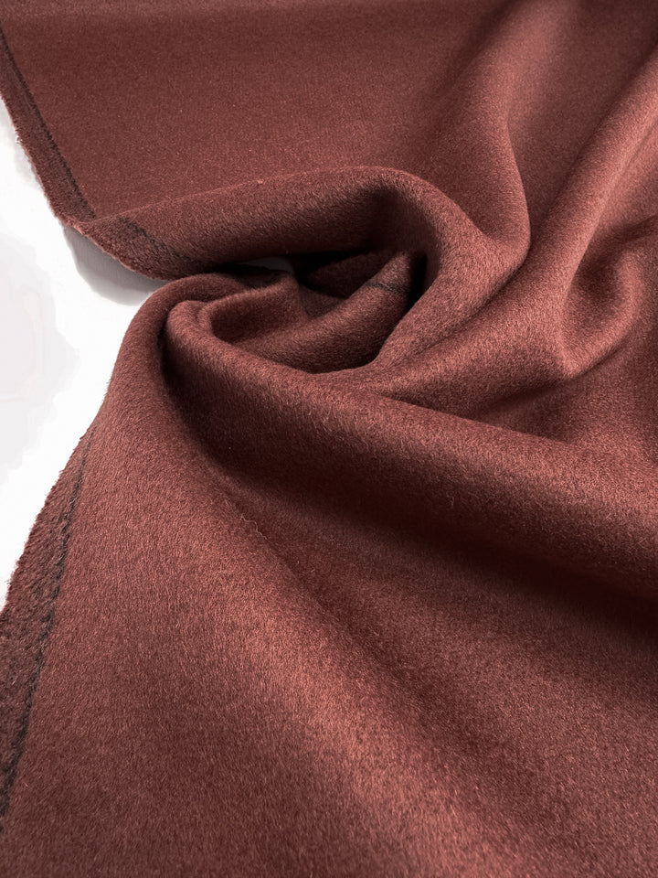 A close-up of Super Cheap Fabrics’ Wool Cashmere - Fired Brick (154cm) shows its soft, reddish-brown fibers with a slightly fuzzy texture, gentle folds, and clean-cut edge with a subtle stitched border for a touch of luxury.