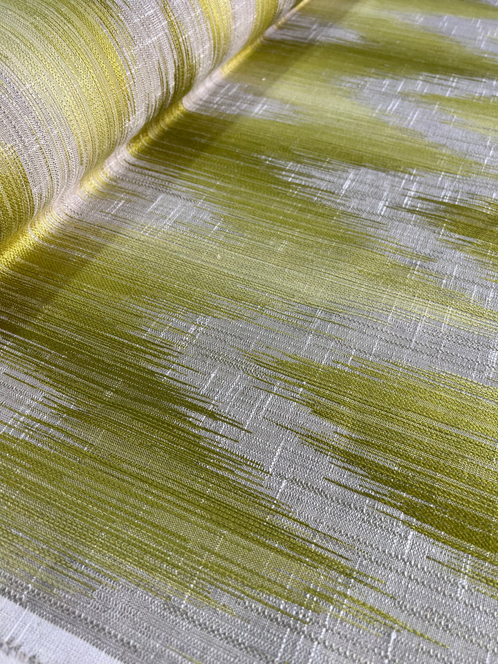 Close-up of an Upholstery Jacquard - Willow - 145cm by Super Cheap Fabrics featuring a modern design with shades of green and white. The texture is visibly coarse, with the green sections appearing as elongated, smudged strokes across the predominantly white background, giving a dynamic, flowing effect. Part of our affordable range.