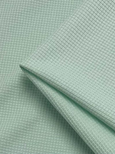 Close-up of a light green, textured waffle fabric with a small waffle pattern. The material is neatly folded to form clean edges, highlighting the intricate texture and soft appearance. The overall look is fresh and uniform. This is the Waffle Knit - Ambrosia - 170cm by Super Cheap Fabrics.