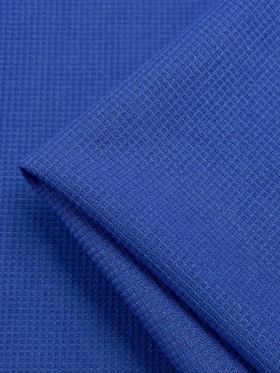Close-up image of a folded piece of Waffle Knit - Royal - 170cm by Super Cheap Fabrics. The fabric has a smooth and three-dimensional appearance, with fine lines creating a subtle checkered design reminiscent of waffle fabric.
