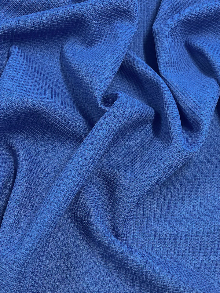 A close-up image of Waffle Knit - Royal - 170cm with a textured, ribbed pattern by Super Cheap Fabrics. The fabric is slightly wrinkled, creating soft folds and shadows that highlight its three-dimensional appearance and intricate weave.