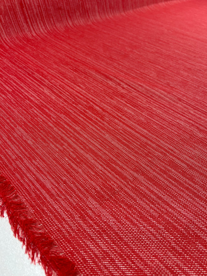 A close-up photo of a red fabric showcasing its woven texture. The Upholstery Twill - Cherry - 147cm from Super Cheap Fabrics, likely for furniture upholstery, has a subtle striped pattern and slightly frayed edges, indicating it may be unfinished. The lighting highlights the threads, enhancing the detail and depth of the material.