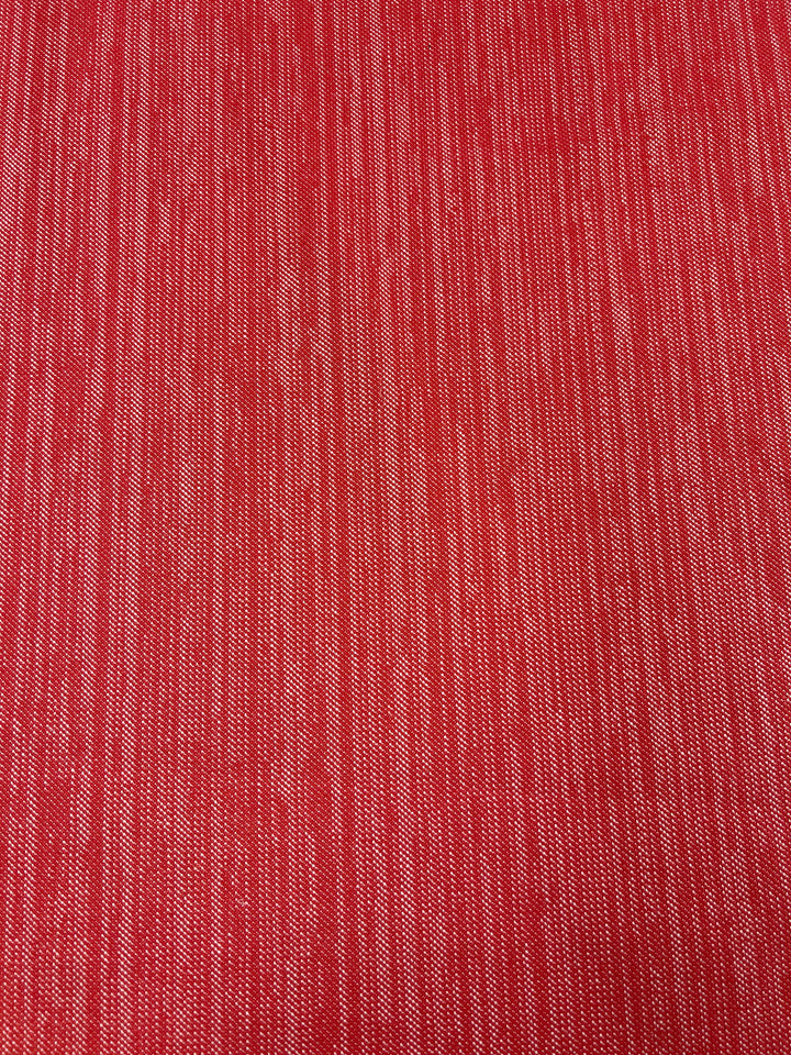 A close-up of a textured red fabric with vertical lines. The material, featuring a twill weave, has a slightly glossy sheen that highlights the subtle pattern created by the weave. Ideal for furniture upholstery, its rich and vibrant appearance adds depth and interest to any surface. This is Upholstery Twill - Cherry - 147cm by Super Cheap Fabrics.
