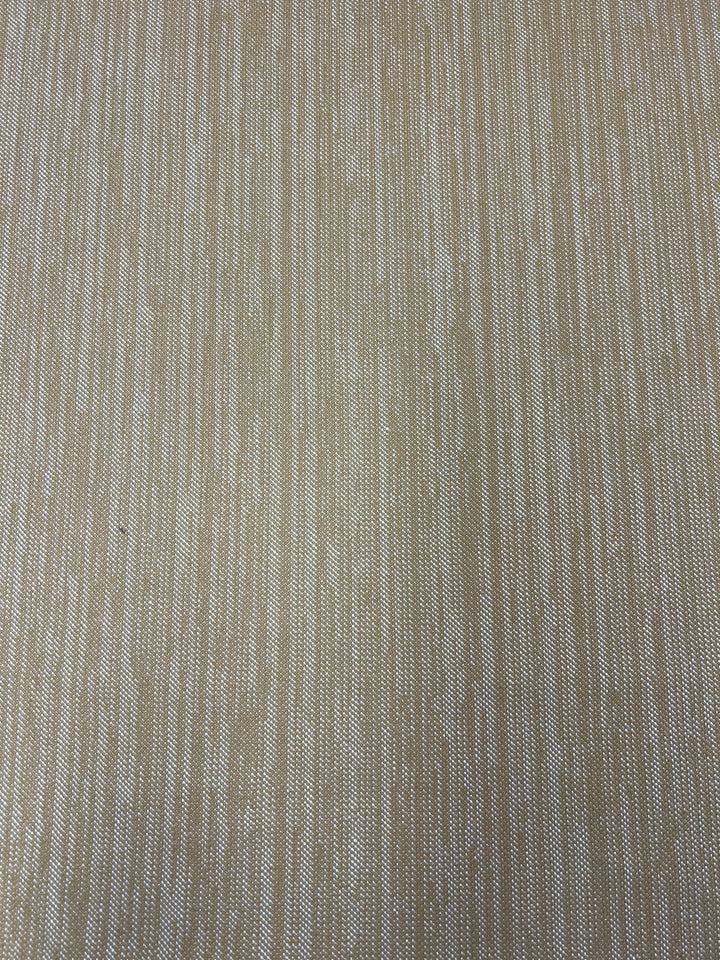 A close-up image of Upholstery Twill - Caramel - 147cm by Super Cheap Fabrics in beige and off-white colors. The pattern consists of vertical streaks and lines, creating a subtle, natural look. The texture appears slightly rough and woven, characteristic of durable fabrics used in upholstery twill applications.