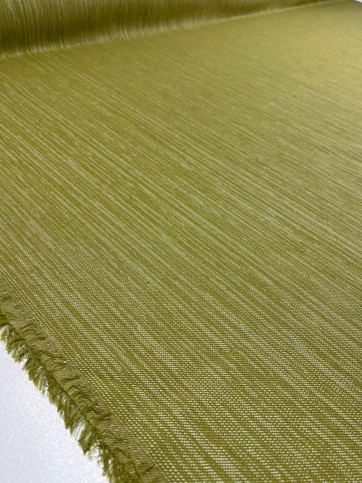 A close-up of a roll of Upholstery Twill - Sweet Pea - 147cm by Super Cheap Fabrics, with a subtle horizontal pattern. The durable twill weave is unrolled on a surface, displaying its slightly frayed edge. The material has a faint sheen, highlighting the weave and texture.