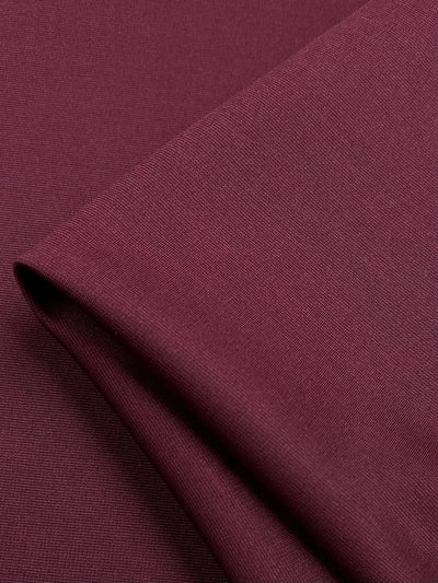 A close-up of a piece of Super Cheap Fabrics' Ponte - Cordovan - 153cm. The smooth and finely woven texture is visible, and a fold in the stretch fabric creates a subtle shadow, highlighting the material's soft and flexible qualities.