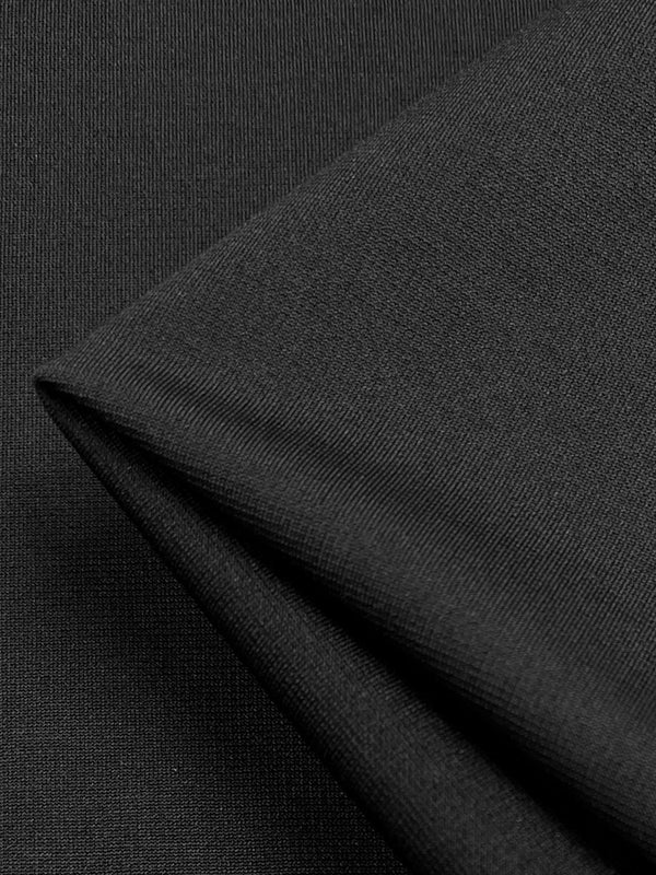 Close-up image of a piece of black ponte fabric, showing a section folded over. The texture of the mid weight knit is smooth with a fine weave, and the lighting highlights subtle variations in its wrinkle-resistant surface. This is Super Cheap Fabrics' Ponte - Black - 150cm.